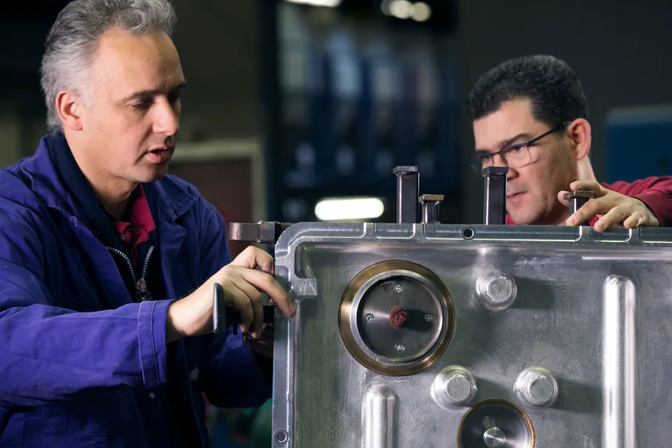 Two colleagues examining the details of a metal mould together.